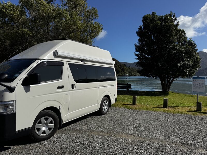 Harriet, a white high-roof Toyota Hiace automatic campervan, parked by the water on a South Island road trip