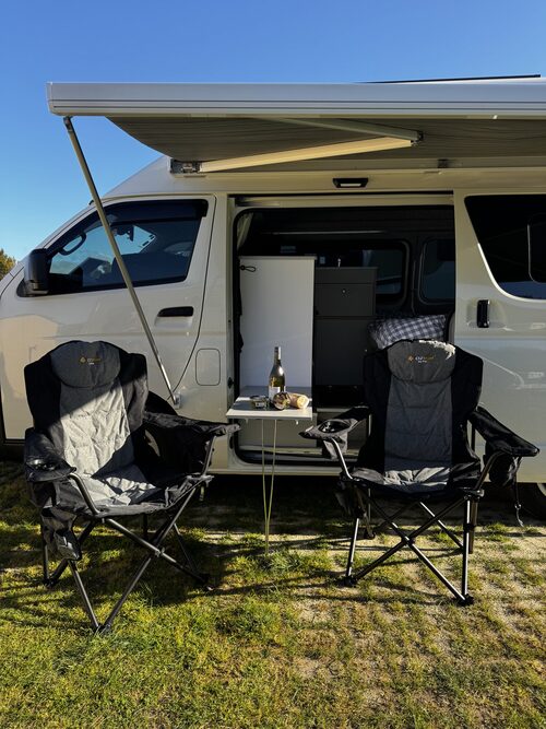 Camping chairs and a table set out under Harriet's awning with the sliding door open