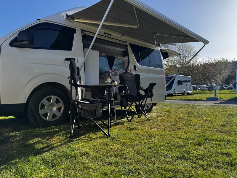 Harriet set up at a campsite with the awning out and two camping chairs and a table on the grass