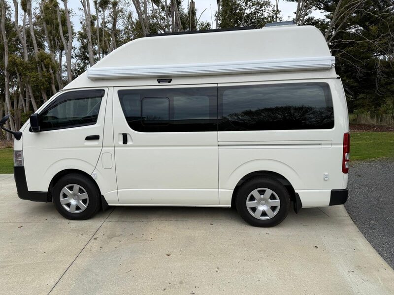 Rear three-quarter view of Harriet showing the high roof and awning box on a 2024 Toyota Hiace